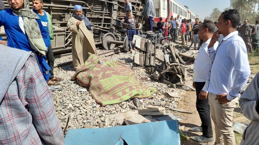 epa09099062 A blanket covers a victim surrounded by people inspecting the scene of a train crash in Sohag province, Egypt, 26 March 2021. At least 32 people were killed and some 66 injured as two pass ...