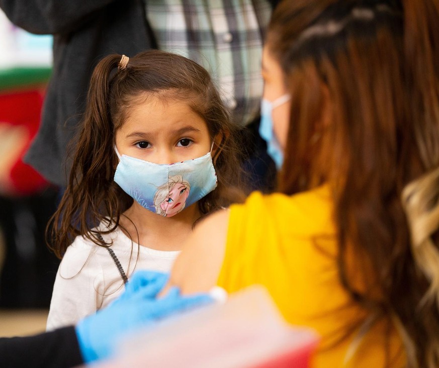 epa09070822 Five year old Brittany Siguenza watches as her mother receives a dose of the Moderna Covid-19 vaccine during a vaccine clinic for teachers and school administrators at the Rumney March Aca ...