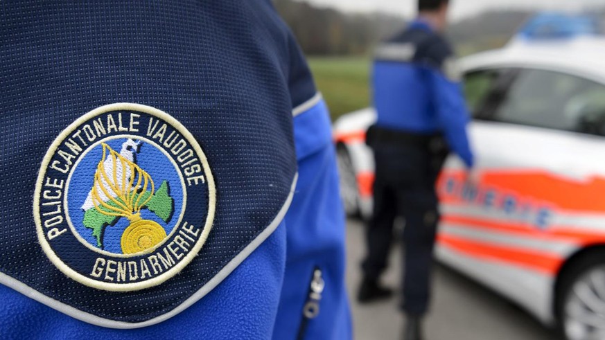 [Editor&#039;s note: photo mise-en-scene] Detail view of the uniform of a police officer of the cantonal police of Vaud, in the foreground, and another cantonal police officer next to a police car, in ...