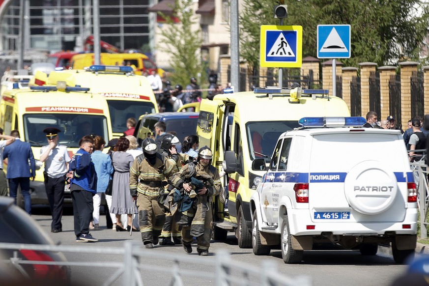 Firefighters walk past ambulances and police cars and a truck parked at a school after a shooting in Kazan, Russia, Tuesday, May 11, 2021. Russian media report that several people have been killed and ...