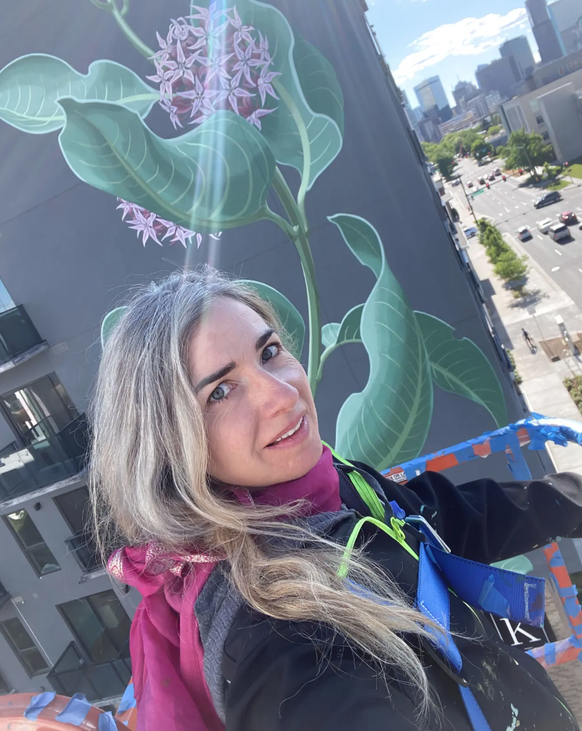 Selfie de Mona Caron devant une plante d'asclépiade créée par l'artiste dans la ville de Denver.