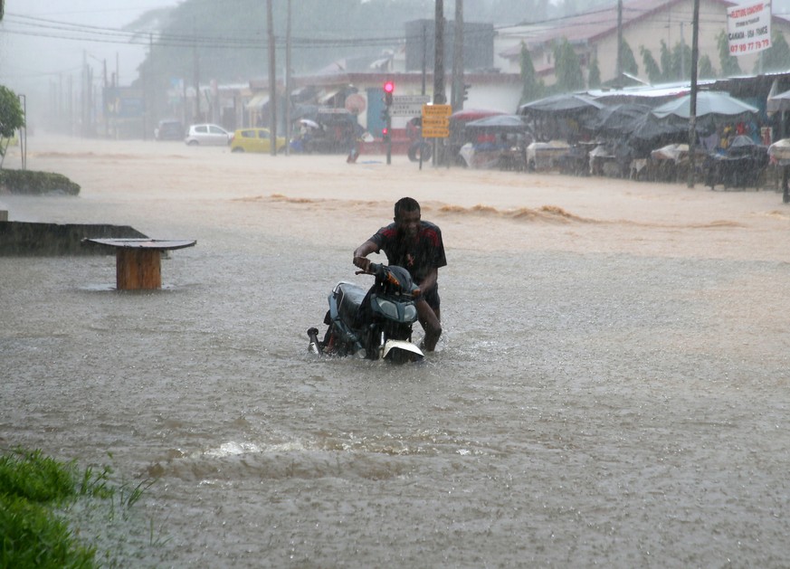 epa11410108 A man pushes a motorbike through a street flooded by heavy rains in Abidjan, Ivory Coast, 14 June 2024. The city of Abidjan has been on high alert since 13 June 2024, as the rainy season w ...