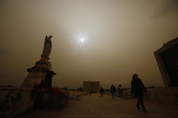 epa09826441 Several passers-by cross the Roman Bridge amid an orange fog blanket caused by airbone dust from Sahara desert in the city of Cordoba, Andalusia, southern Spain, 15 March 2022. A wave of a ...