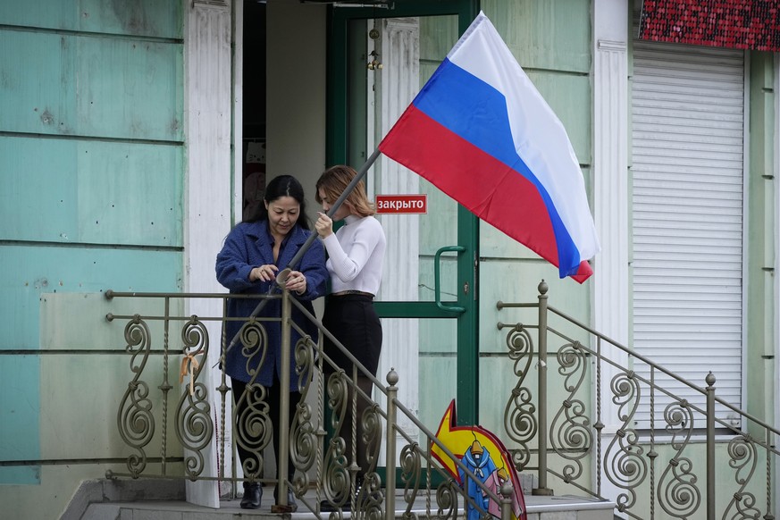 Women hang a Russian flag at their shop a day after voting in four Moscow-held regions of Ukraine on referendums to become part of Russia, in Luhansk, Luhansk People&#039;s Republic controlled by Russ ...