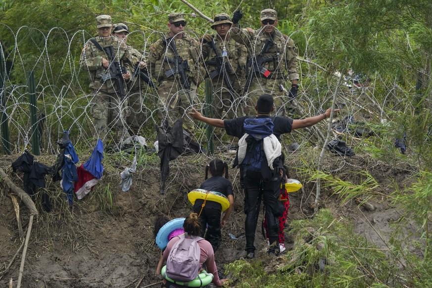 Un migrant sur le sol mexicain fait un geste vers les gardes nationaux du Texas, derrière des barbelés.