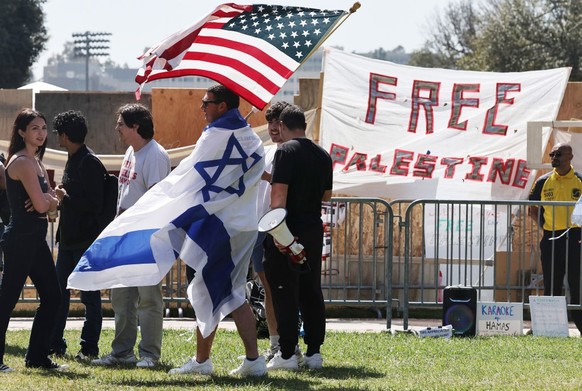 LOS ANGELES, CALIFORNIA - APRIL 30: A counter-demonstrator wears an Israeli flag while carrying an American flag near a pro-Palestinian encampment at the University of California, Los Angeles (UCLA) c ...