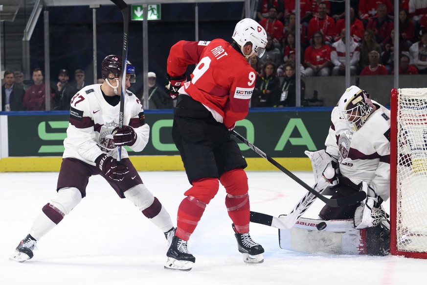 Switzerland's Damien Riat, center, vies for the puck against Latvia's goaltender Kristers Gudlevskis, right, and Latvia's Oskars Lapinskis, left, during the 2026 IIHF Men's Ice Hoc ...