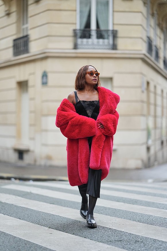 PARIS, FRANCE - DECEMBER 18: Carrole Sagba wears shoulder-length straight brown bob hair with a center part, makeup with an even complexion, defined brows and deep red lipstick, narrow brown-tinted su ...