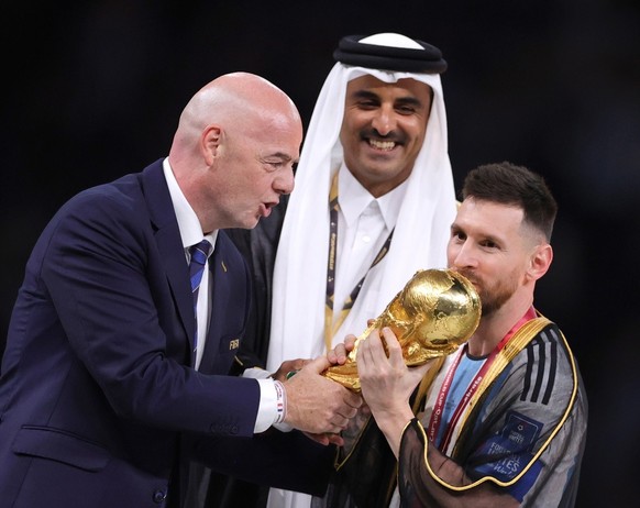 epa10373046 Lionel Messi (R) of Argentina celebrates with the World Cup trophy next to Tamim bin Hamad Al Thani (C), the Emir of Qatar, and FIFA President Gianni Infantino (L) during the trophy ceremo ...