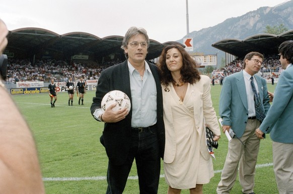 Der Schauspieler Alain Delon steht mit einem Fussball und in weiblicher Begleitung neben dem Spielfeld im Stade de Tourbillon in Sion. Aufgenommen an der Meisterfeier des FC Sion im Mai 1992. (KEYSTON ...