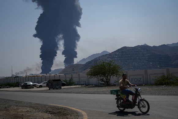 FILE - A man rides a bike as fires and plumes of smoke rise after debris from an intercepted Iranian drone struck an oil facility, according to authorities, in Fujairah, United Arab Emirates, March 14 ...