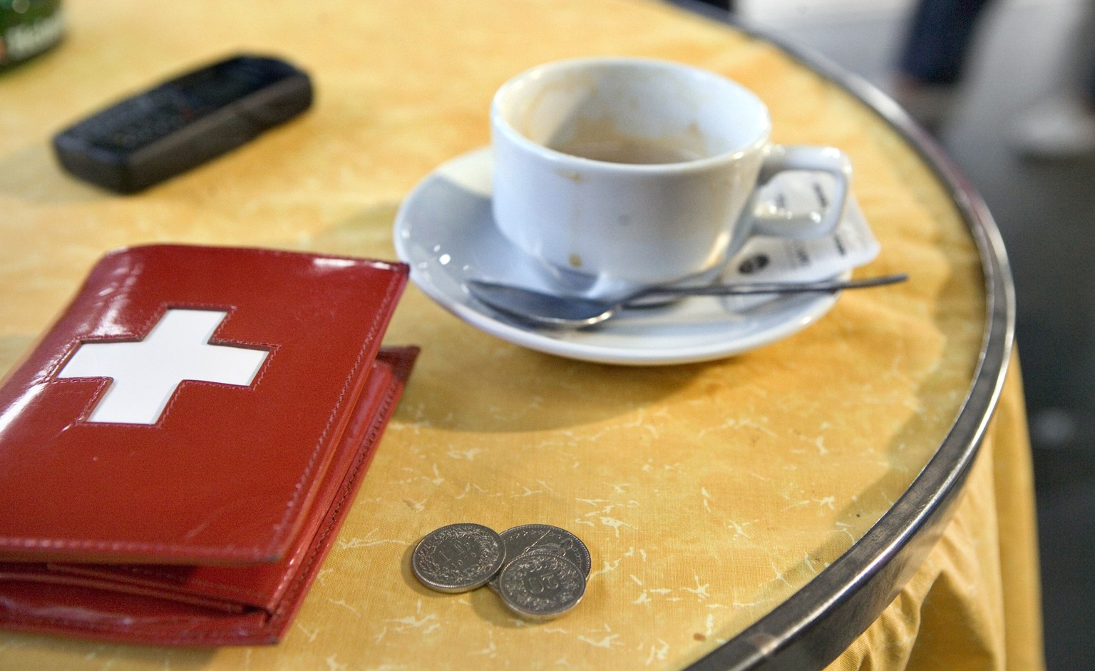 Ein Portemonnaie mit einem Schweizer Kreuz, eine Kaffeetasse, ein Handy und ein paar Muenzen in einem Restaurant im Hauptbahnhof Zuerich, aufgenommen am 24. Oktober 2005. (KEYSTONE/Martin Ruetschi)

A ...