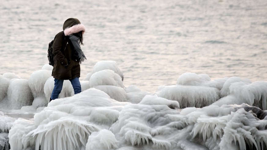epa06569029 A woman walks on the pier that is covered with ice after few days of strong gusts of wind blowing waves of water over the bank of the lake of Geneva, in Geneva, Switzerland, 27 February 20 ...