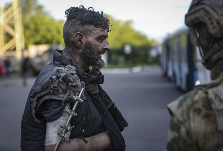 epa09953883 Self-proclaimed DPR militia (R) watches an Ukrainian serviceman boarding a bus as he is being evacuated from the besieged Azovstal steel plant in Mariupol, Ukraine, 17 May 2022. A total of ...