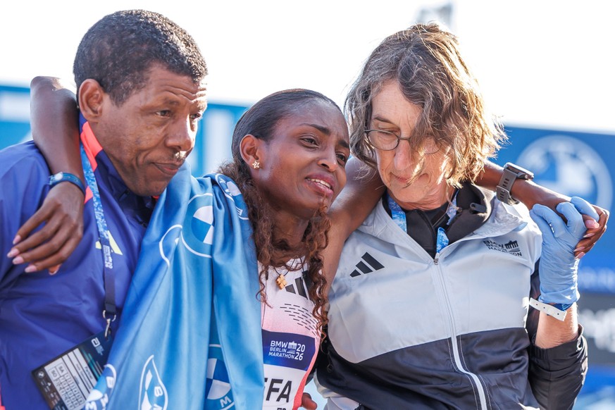 27.09.2026, Berlin: Leichtathletik: Marathon. Tigst Assefa (M, Äthiopien) läuft beim BMW Berlin Marathon als Erste durchs Ziel. Sie muss danach wegen ihrer Krämpfe gestützt werden.....Die Läuferin hat ...