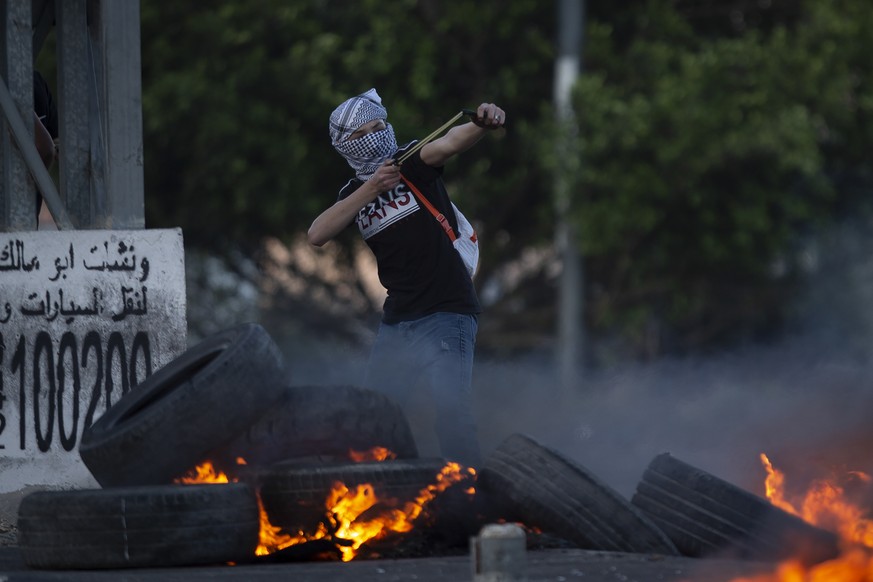 A masked Palestinian protester uses a slingshot during clashes with Israeli troops at the Hawara checkpoint, south of the West Bank city of Nablus, Monday, May 17, 2021. (AP Photo/Majdi Mohammed)
