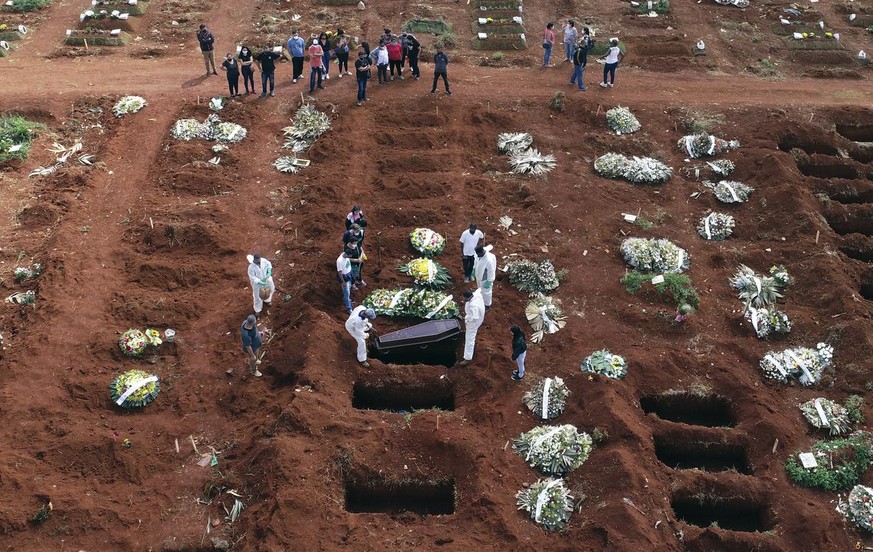 Cemetery workers wearing protective gear lower the coffin of a person who died from complications related to COVID-19 into a gravesite at the Vila Formosa cemetery in Sao Paulo, Brazil, Wednesday, Apr ...