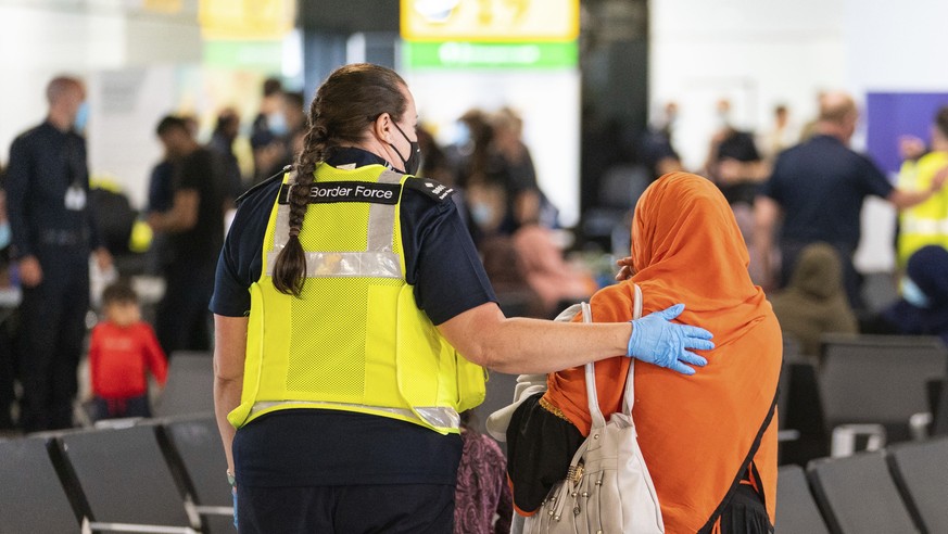 A member of Border Force staff assists a female evacuee from Afghanistan who arrived aboard an evacuation flight at Heathrow Airport in London, Thursday Aug. 26, 2021. The U.K. defense ministry has or ...