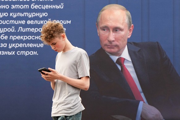 A young man walks past a poster with an image of Russian President Vladimir Putin and a quote from his message at an annual book fair in St. Petersburg, Russia, Thursday, May 21, 2026. (AP Photo/Dmitr ...