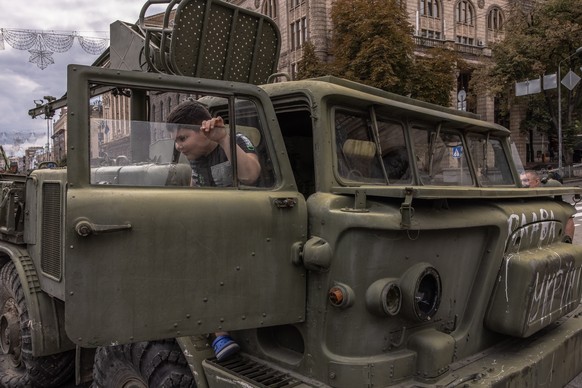 epa10130436 A boy sits in a Russian military vehicle that was damaged in fights with the Ukrainian army, displayed on Khreshchatyk street, in downtown Kyiv, ahead of the 'Independence Day', ...
