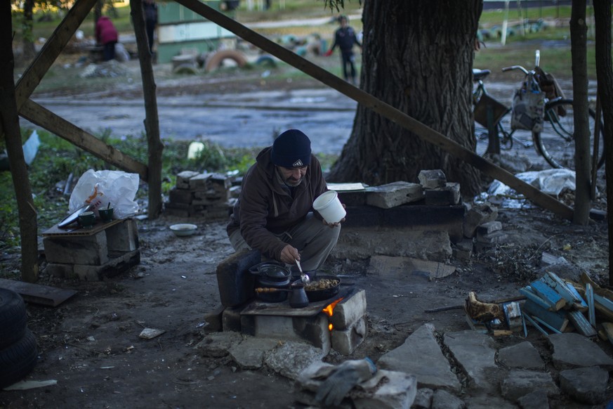 A man cooks on a makeshift stove in Kivsharivka, Ukraine, Sunday, Oct. 16, 2022. Residents in Kivsharivka have been living with no gas, electricity or running water supply for around three weeks. (AP  ...