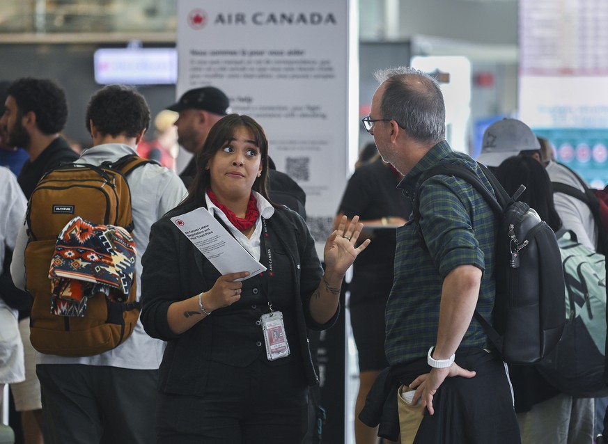 An Air Canada agent, left, talks with a man as Air Canada flight attendants strike at Montreal-Pierre Elliott Trudeau International Airport in Montreal, Saturday, Aug. 16, 2025. (Graham Hughes/The Can ...
