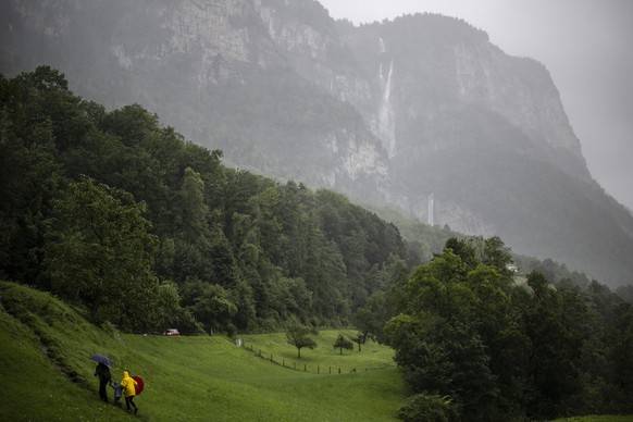 Menschen mit Schirm sind unterwegs zu den Seerenbachfaelle, am Montag, 28. Juli 2025, bei Betlis in Amden. Die Seerenbachfaelle fuehren ueber drei Stufen und haben eine Gesamthoehe von 585 Metern. Im ...