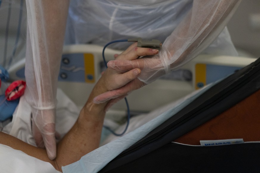 A Nurse holds the hand of a COVID-19 patient on a ventilator in the COVID-19 intensive care unit at the la Timone hospital in Marseille, southern France, Friday, Dec. 31, 2021. Paris region health aut ...
