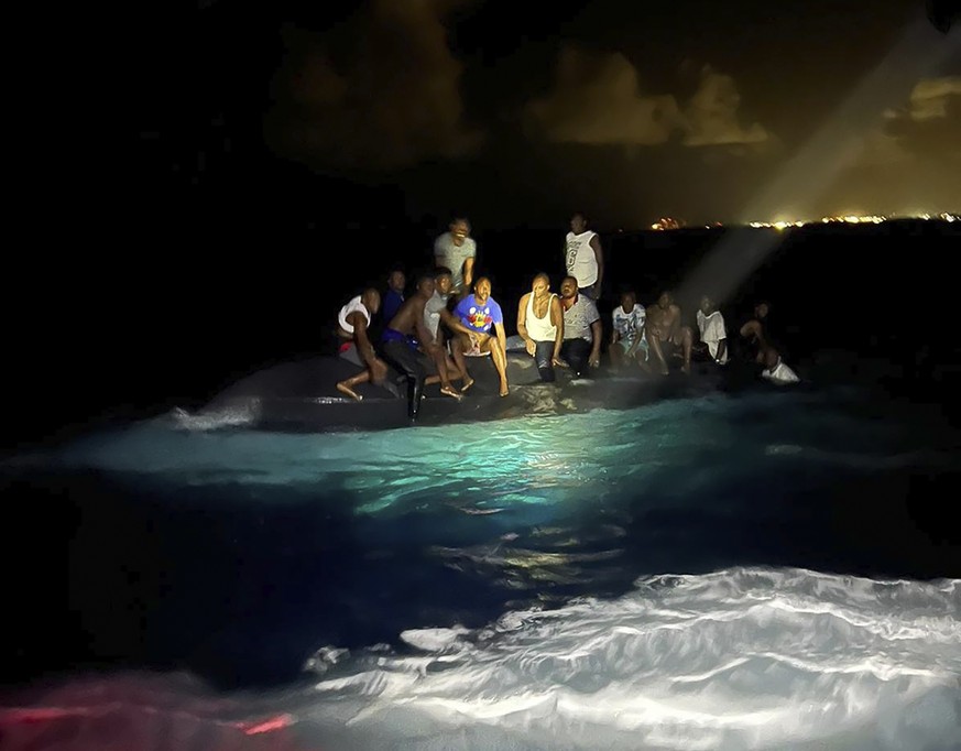 In this photo provided by the Royal Bahamas Defense Force, survivors sit on a capsized boat as they are about to be rescued near New Providence in the Bahamas, early Sunday, July 24, 2022. Bahamas Pri ...