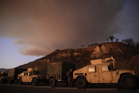 California National Guard line up along the Pacific Coast Highway as a plume of smoke rises from the Palisades Fire on Friday, Jan. 10, 2025, in the Pacific Palisades section of Los Angeles. (AP Photo ...