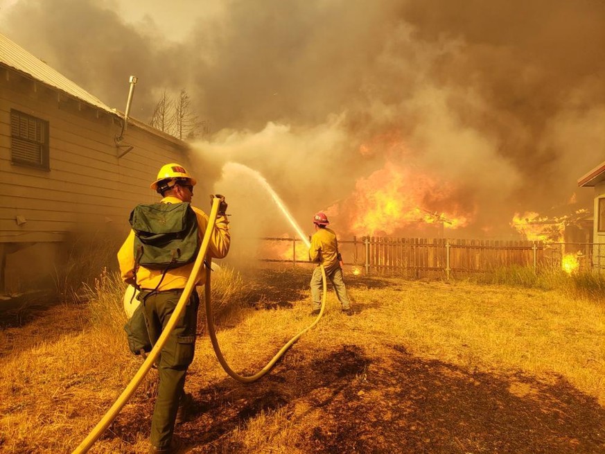 epa09399895 A handout photo made available by the US Forest Service (USFS) shows firefighters working to protect a home from the flames in Greenville, California, USA, 05 August 2021 (issued 06 August ...