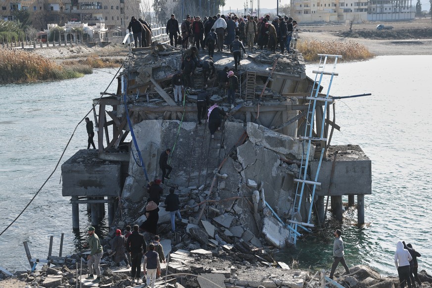 FILE - People climb over the damaged Al-Rashid Bridge, with some crossing on foot, after it was destroyed as Kurdish-led Syrian Democratic Forces withdrew, a day after Syrian government forces took co ...