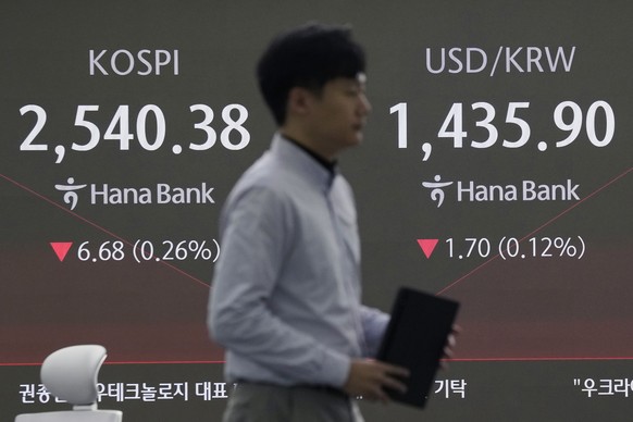 A currency trader passes by a screen showing the Korea Composite Stock Price Index (KOSPI), left, and the foreign exchange rate between U.S. dollar and South Korean won at the foreign exchange dealing ...