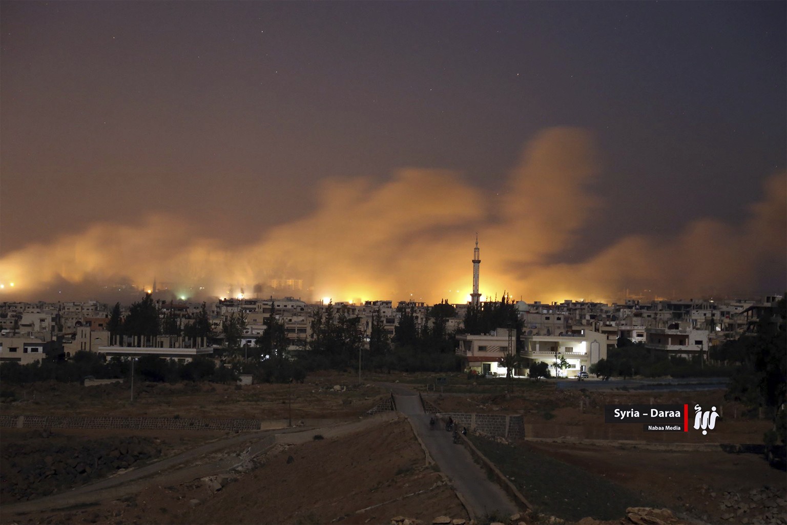 This photo provided Monday, June 25, 2018, by Nabaa Media, a Syrian opposition media outlet, shows smoke rising over buildings that were hit by Syrian government forces bombardment, in Busra al-Harir, ...