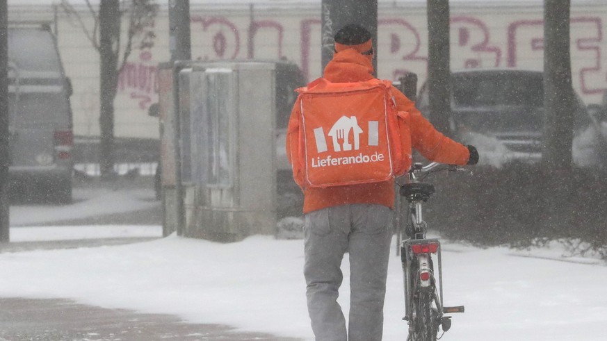 epa08993500 A food delivery man of Lieferando pushes his bike in a snowstorm along a main road in Bremen, northern Germany, 07 February 2021. A heavy winter storm with cold easterly winds brings ice a ...