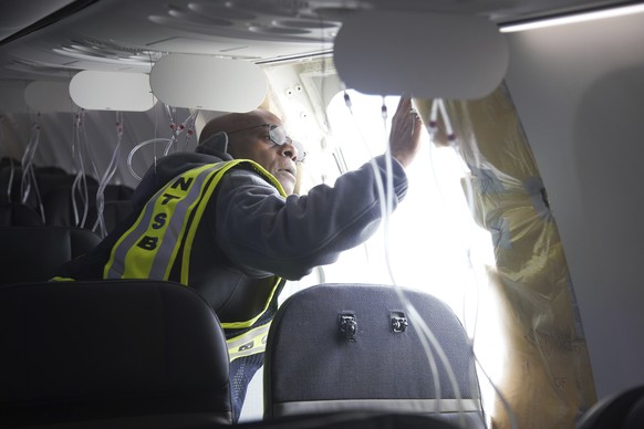 This image taken Sunday, Jan. 7, 2024, and released by the National Transportation Safety Board, an investigator examines the frame on a section of Alaska Airlines Flight 1282 that is missing panel on ...