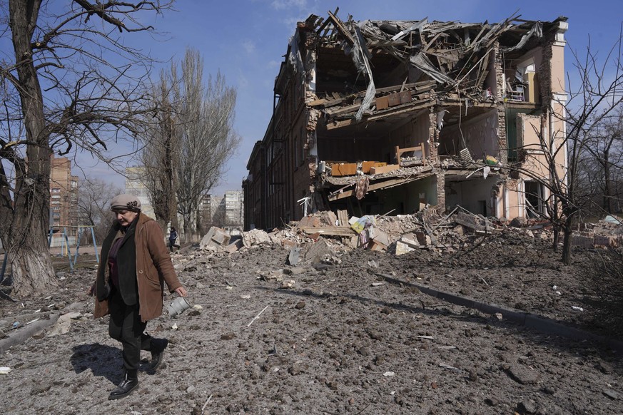 A woman walks past building damaged by shelling in Mariupol, Ukraine, Sunday, March 13, 2022. The surrounded southern city of Mariupol, where the war has produced some of the greatest human suffering, ...