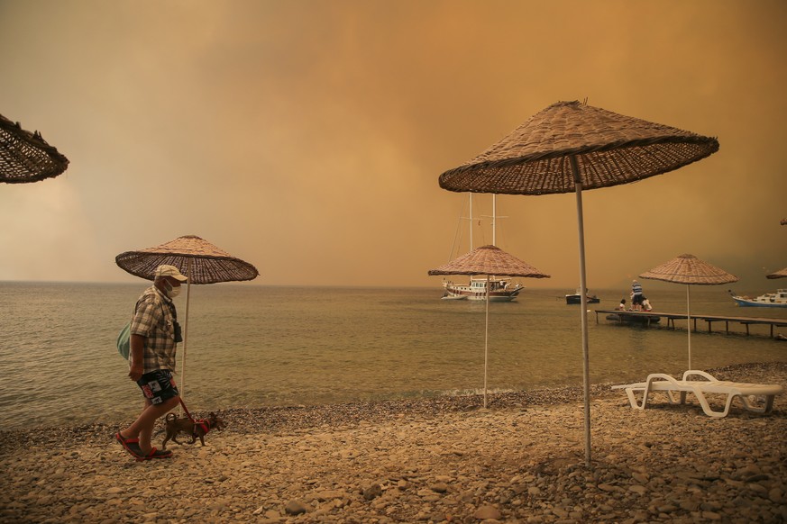 A man walks with his dog on the beach of smoke-engulfed Mazi area as wildfires rolled down the hill toward the seashore, in Bodrum, Mugla, Turkey, Sunday, Aug. 1, 2021. More than 100 wildfires have be ...