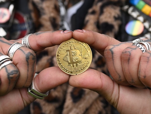 epaselect epa09600698 A performer holds a metal representation of a Bitcoin during a photocall in front of the Tower of London in London, Britain, 24 November 2021. The photocall was organized to cele ...