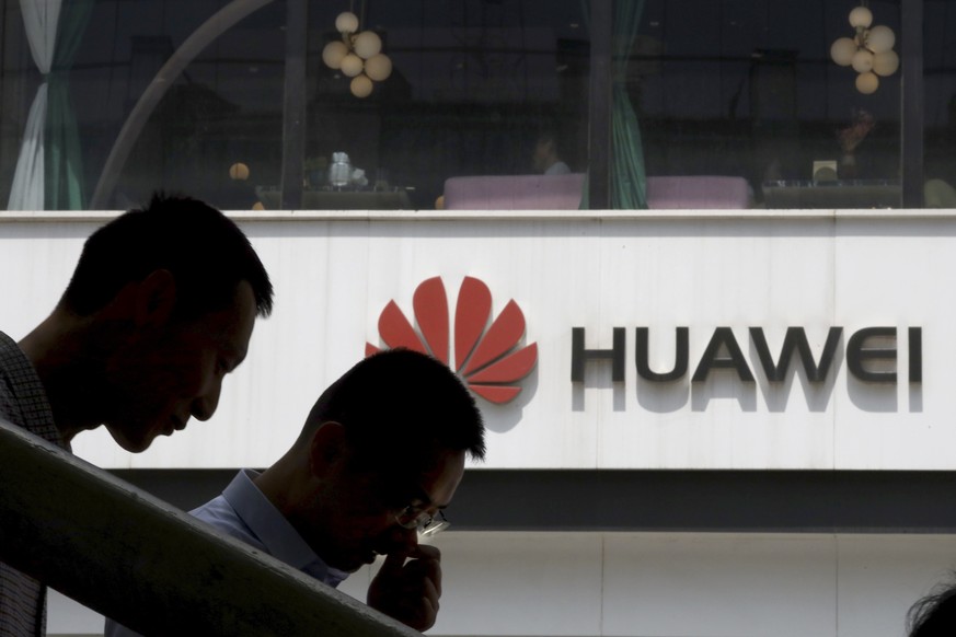 In this May 16, 2019, photo, Chinese men pass by a Huawei retail shop in Beijing. Stepping up the pressure on Beijing, the U.S. Commerce Department has effectively barred U.S. companies from selling o ...