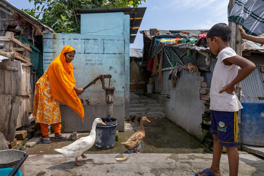 Eine Frau pumpt Wasser aus dem Brunnen im Slum Bastuhara in Bangladesch