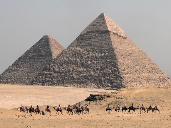 epa09489095 People ride camels past the pyramids in Giza, Egypt, 23 September 2021 (issued 26 September 2021). The United Nations (UN) World Tourism Day 2021 is observed on 27 September and this year ...