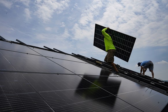 FILE - Nicholas Hartnett, owner of Pure Power Solar, carries a panel as he and Brian Hoeppner, right, install a solar array on the roof of a home in Frankfort, Ky., July 17, 2023. A business group tha ...