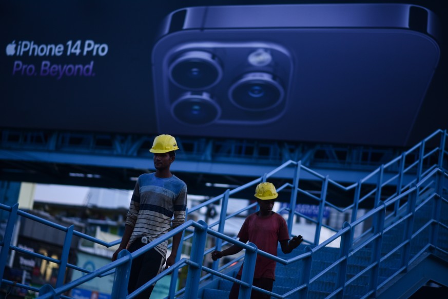 epa10180007 Indian laborers walk down a pedestrian bridge as they pass in front of an Apple iPhone 14 pro advertisement billboard, in Chennai, India, 12 September 2022. Tata Group is reportedly in tal ...