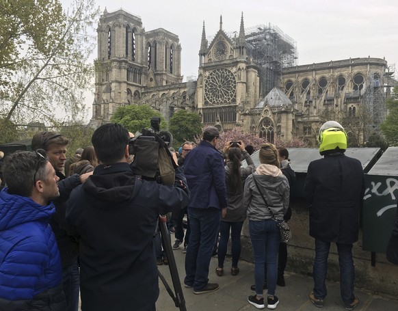 People watch Notre Dame cathedral Tuesday April 16, 2019 in Paris. Experts assessed the blackened shell of Paris' iconic Notre Dame Tuesday morning to establish next steps to save what remains after a devastating fire destroyed much of the cathedral that had survived almost 900 years of history. (AP Photo/Samuel Petrequin)
