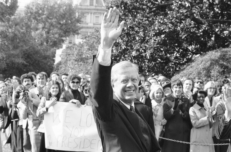 FILE - U.S. President Jimmy Carter waves as staff holds up sign proclaiming &quot;We Love you Mr. President&quot; in Washington, Nov. 5, 1980, as the president walks to helicopter for trip to Camp Dav ...