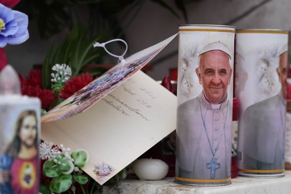Candles with the pictures of Pope Francis are the laid under the statue of late Pope John Paul II outside Agostino Gemelli Polyclinic in Rome, Wednesday, Feb. 19, 2025, where the Pontiff is hospitaliz ...