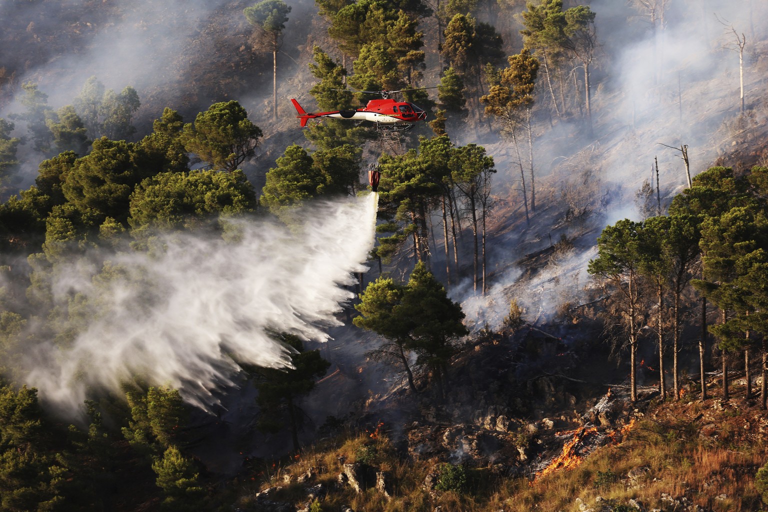 A firefighting helocopter drains water on a wildfire on the mountain in Altofonte near Palermo, Italy, Wednesday, July 26, 2023. Firefighters battled wildfires across southern Italy as searing tempera ...
