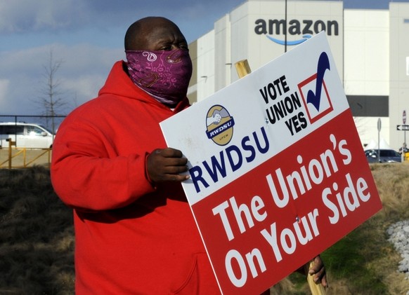 FILE - In this Tuesday, Feb. 9, 2021, file photo, Michael Foster of the Retail, Wholesale and Department Store Union holds a sign outside an Amazon facility where labor is trying to organize workers i ...