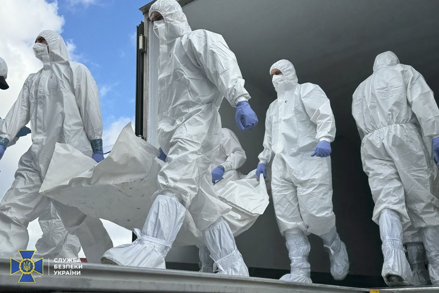 epa12387343 A handout photo made available by the Security Service of Ukraine (SBU) shows Ukrainian special team members wearing hazmat suits during the repatriation of the bodies of fallen Ukrainian  ...